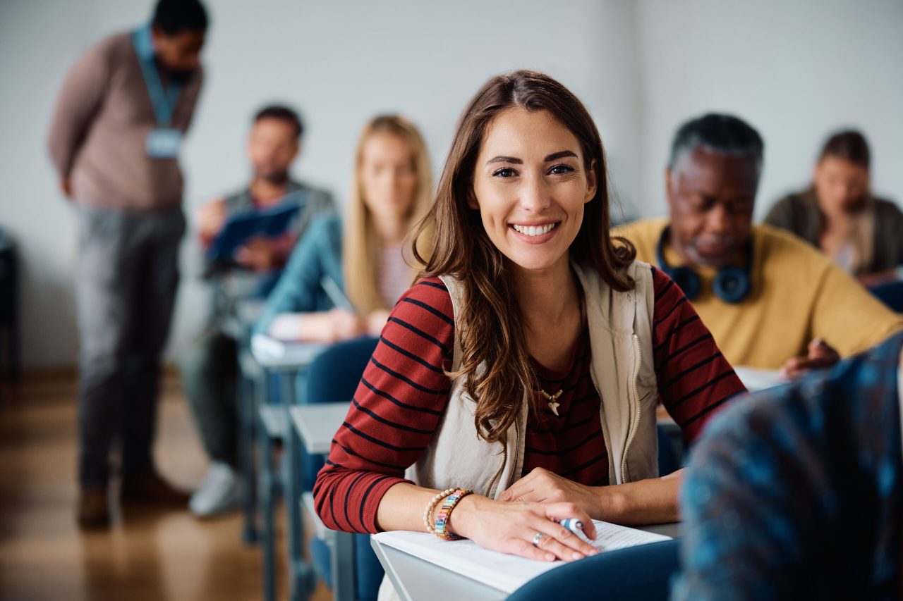 Young happy woman attending adult education training class in lecture hall and looking at camera.